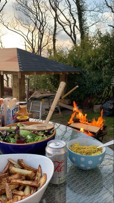 a table topped with bowls filled with food next to a fire pit on top of a patio