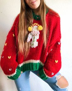 a woman wearing a red sweater with flowers on it is posing in front of a white wall