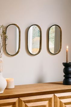 three mirrors on the wall above a dresser with a vase and candle next to it