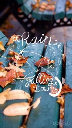 the words rain is falling down are written on an old wooden bench with fallen leaves