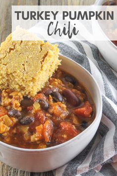 a bowl of turkey pumpkin chili with cornbread on the side and a spoon in it