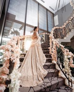 a woman in a wedding dress is standing on some stairs with flowers and greenery