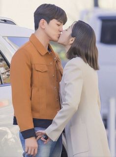 a man and woman kissing in front of a car