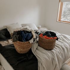 an unmade bed with two baskets full of clothes on top of it and a window in the background