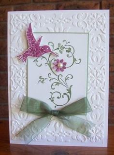 a white card with a pink bird on it and green ribbon around the edge, sitting on a wooden table