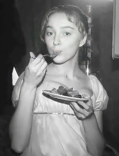 black and white photograph of a woman eating food from a plate in front of her