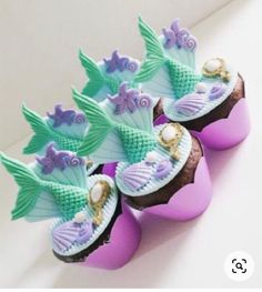 three cupcakes with mermaid decorations on them are sitting next to eachother