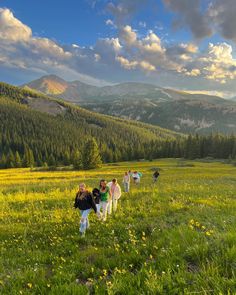 a group of people walking across a lush green field with mountains in the background on a sunny day