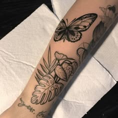 a woman's arm with a butterfly and flowers tattoo on it