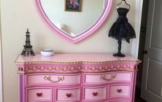 a pink dresser with an ornate mirror on the wall above it and a mannequin standing next to it