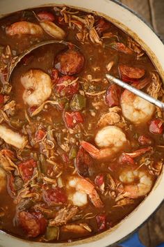 a pot filled with shrimp, sausage and tomato soup on top of a wooden table