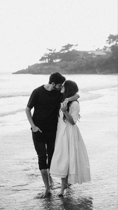 a man and woman are standing in the water at the edge of the beach with their arms around each other