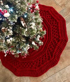 a red knitted christmas tree skirt sitting on top of a wooden floor next to a white christmas tree