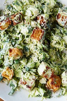 a white plate topped with shaved cabbage and croutons next to a bowl of dressing