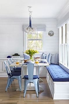 a dining room table with blue chairs and a bench in front of the window,