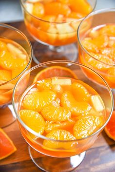 four glasses filled with oranges and slices on top of a wooden table next to sliced fruit