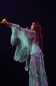 a woman with red hair and green dress holding a yellow flower in her right hand