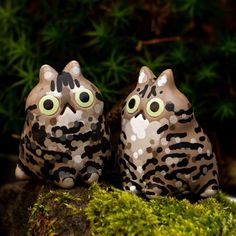 two ceramic owls sitting on top of a moss covered rock with eyes painted on them