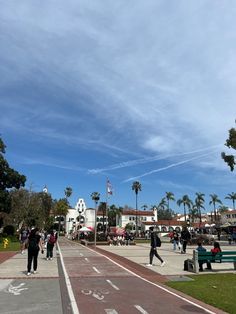 people are walking around in the park on a sunny day with palm trees and blue skies