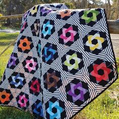 a quilted blanket sitting on top of a grass covered field next to a fence