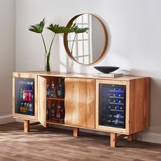 a wooden sideboard with two wine bottles and a plant in it next to a round mirror