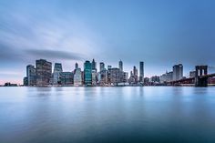 the city skyline is shown from across the water at dusk with blue sky and clouds