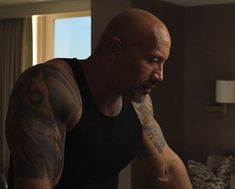 a bald man with tattoos on his arm and chest standing in front of a bed