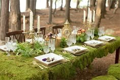 a moss covered table with candles and plates on it