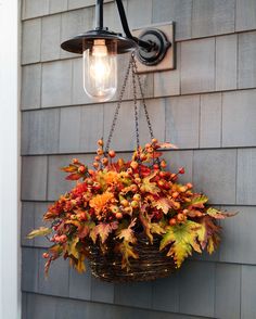 a hanging basket filled with autumn leaves on the side of a house next to a light