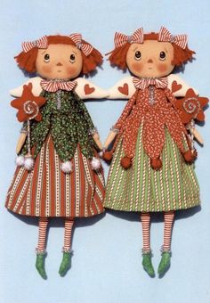 two dolls are standing next to each other on a blue background, one is wearing a red and green dress