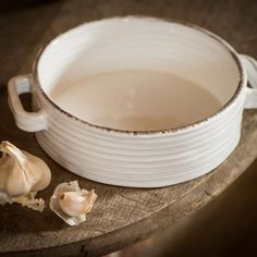 a white bowl sitting on top of a wooden table next to garlic cloves