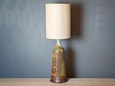 a lamp sitting on top of a wooden table next to a blue wall with a painting on it