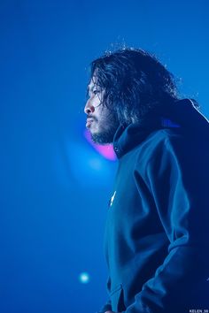 a man with long hair standing in front of a blue background