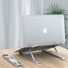 an apple computer sitting on top of a wooden desk next to a remote control and plant