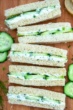 cucumber and dill pickle sandwiches on a wooden cutting board with sliced cucumbers