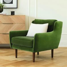 a green chair sitting on top of a hard wood floor next to a white pillow