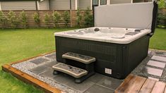 a hot tub sitting on top of a wooden platform next to a green yard and fence