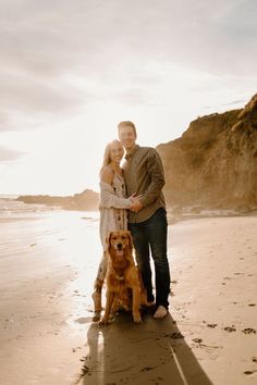 a man and woman standing on the beach with their dog