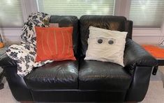 a black leather couch with orange and white pillows on it in front of a window