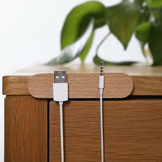 an iphone charger plugged into the side of a wooden cabinet with a plant in the background