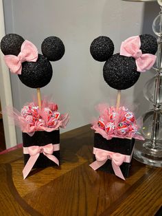 two mickey mouse heads with pink bows and candy in them on top of a table