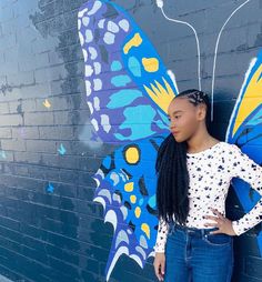 a woman standing in front of a wall with a butterfly painted on it's side