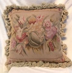 a decorative pillow with tasselled edges and flowers on it sitting on a bed