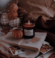 a candle sitting on top of an open book next to some pictures and pumpkins