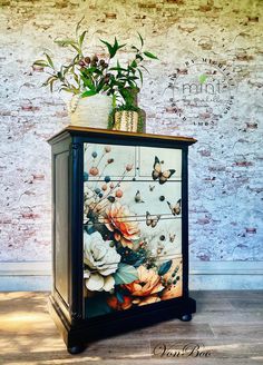 a painted cabinet with flowers and butterflies on the front, against a white brick wall