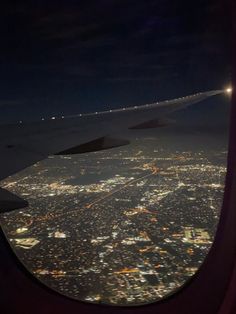 an airplane wing at night with the city lights lit up in the distance as seen from above