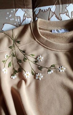 a sweater with white flowers on it laying on a bed next to pillows and blankets