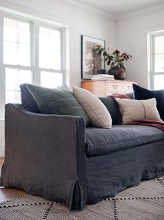 a living room filled with furniture and pillows on top of a wooden floor next to two windows