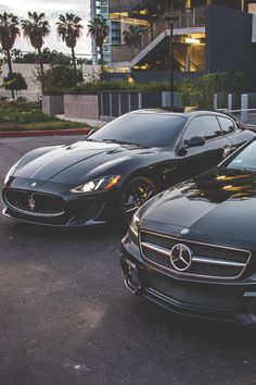 two black sports cars parked next to each other in front of a building with palm trees