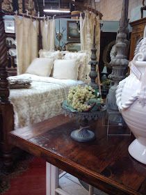 there is a large white vase sitting on a table in front of a bed and dresser